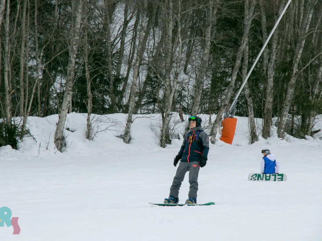 Snowboarder auf der Waldpiste, daneben ein Kind.